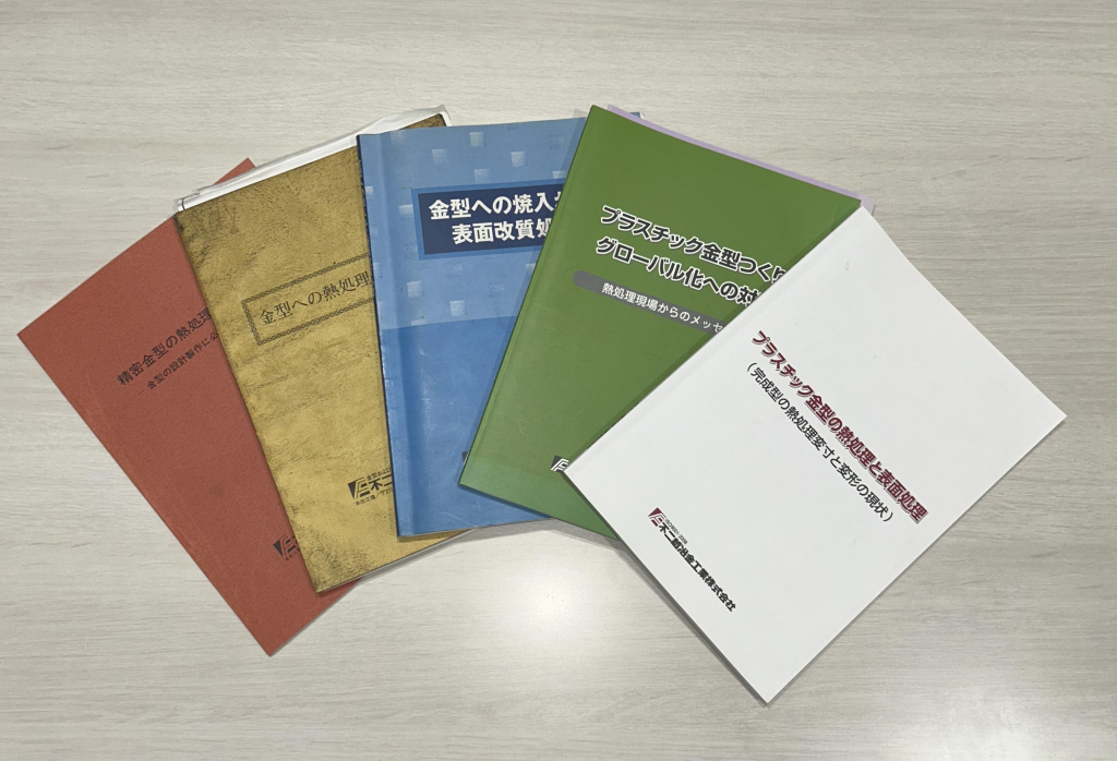 Five Japanese-language books fanned out on a light wooden tabletop, showing red, gold, blue, green, and white covers.